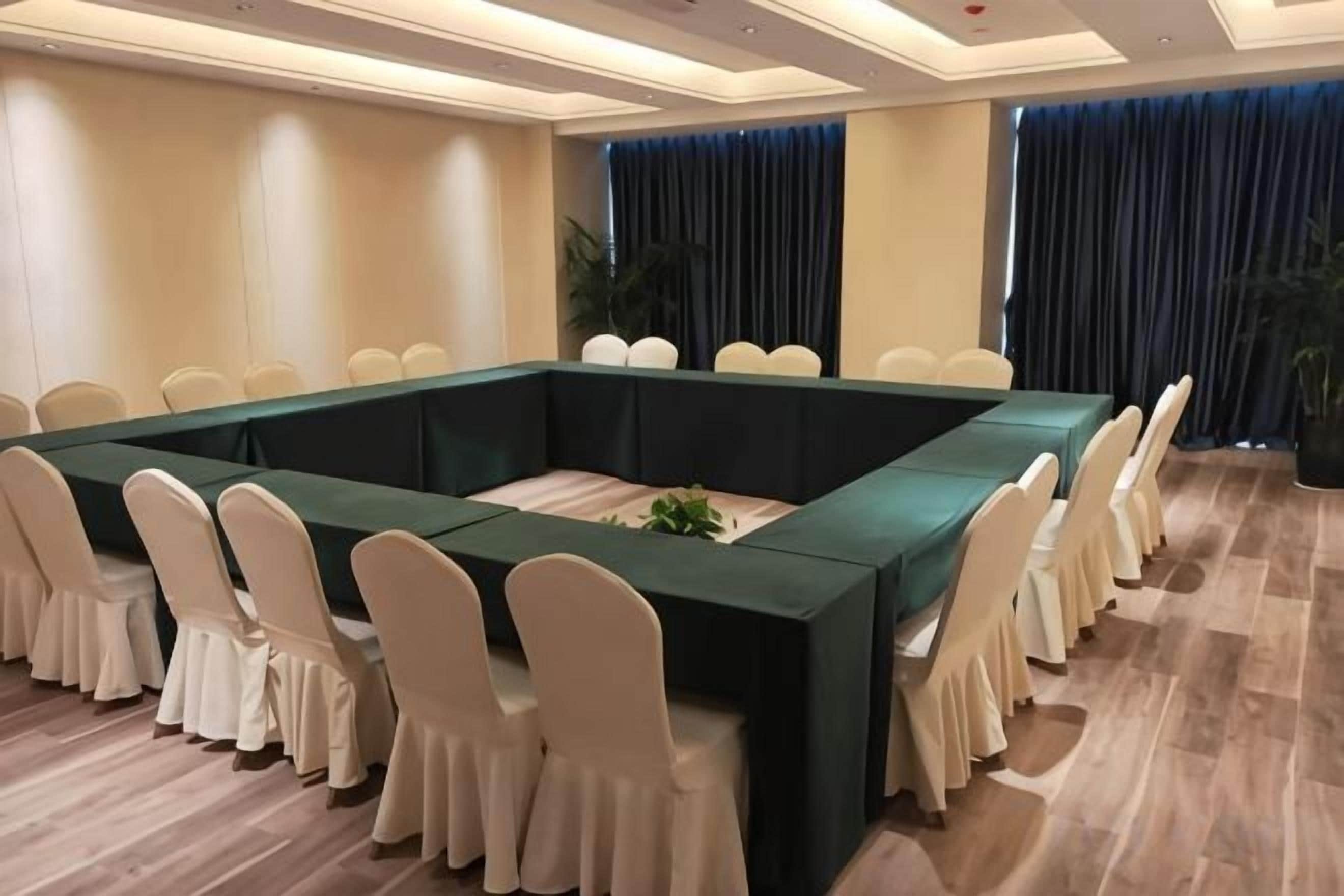 Een vergaderruimte met een lange tafel, witte stoelen en een groene tafelkleed.