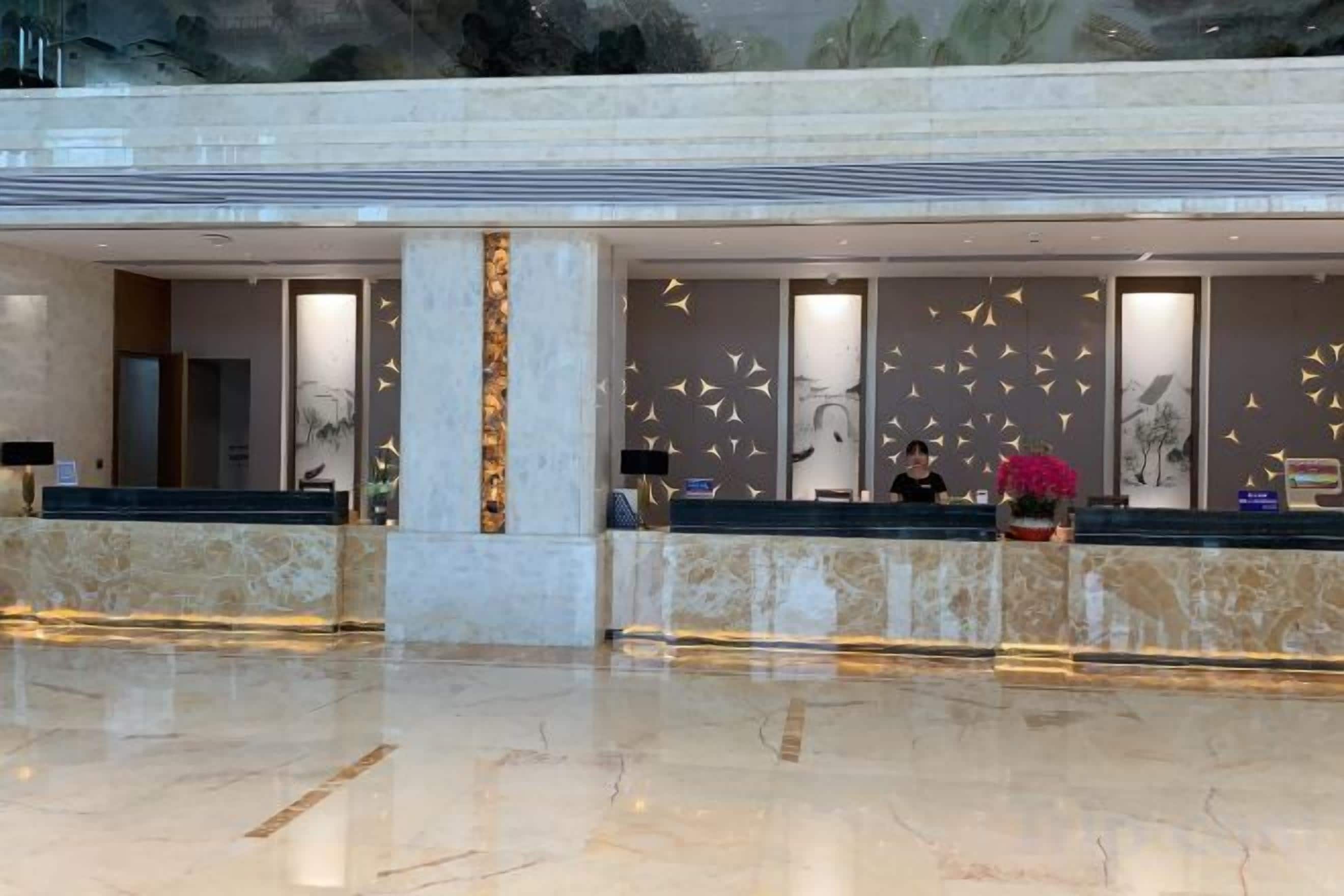 A hotel reception area with marble flooring, a reception desk, and a large window.
