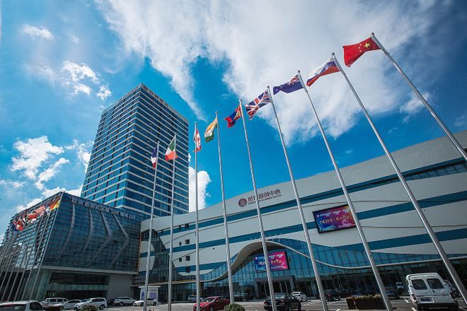 A modern building with multiple flags, a large digital screen, and a clear blue sky.