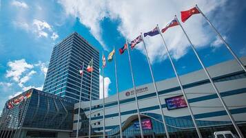 A modern building with multiple flags, a large digital screen, and a clear blue sky.