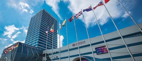 A modern building with multiple flags, a large digital screen, and a clear blue sky.
