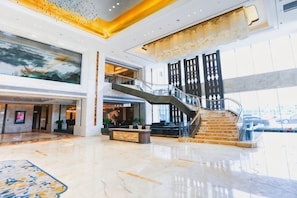 Eine geräumige Lobby mit Marmorboden, einem Empfangstresen, einer Treppe und einem großen Gemälde.