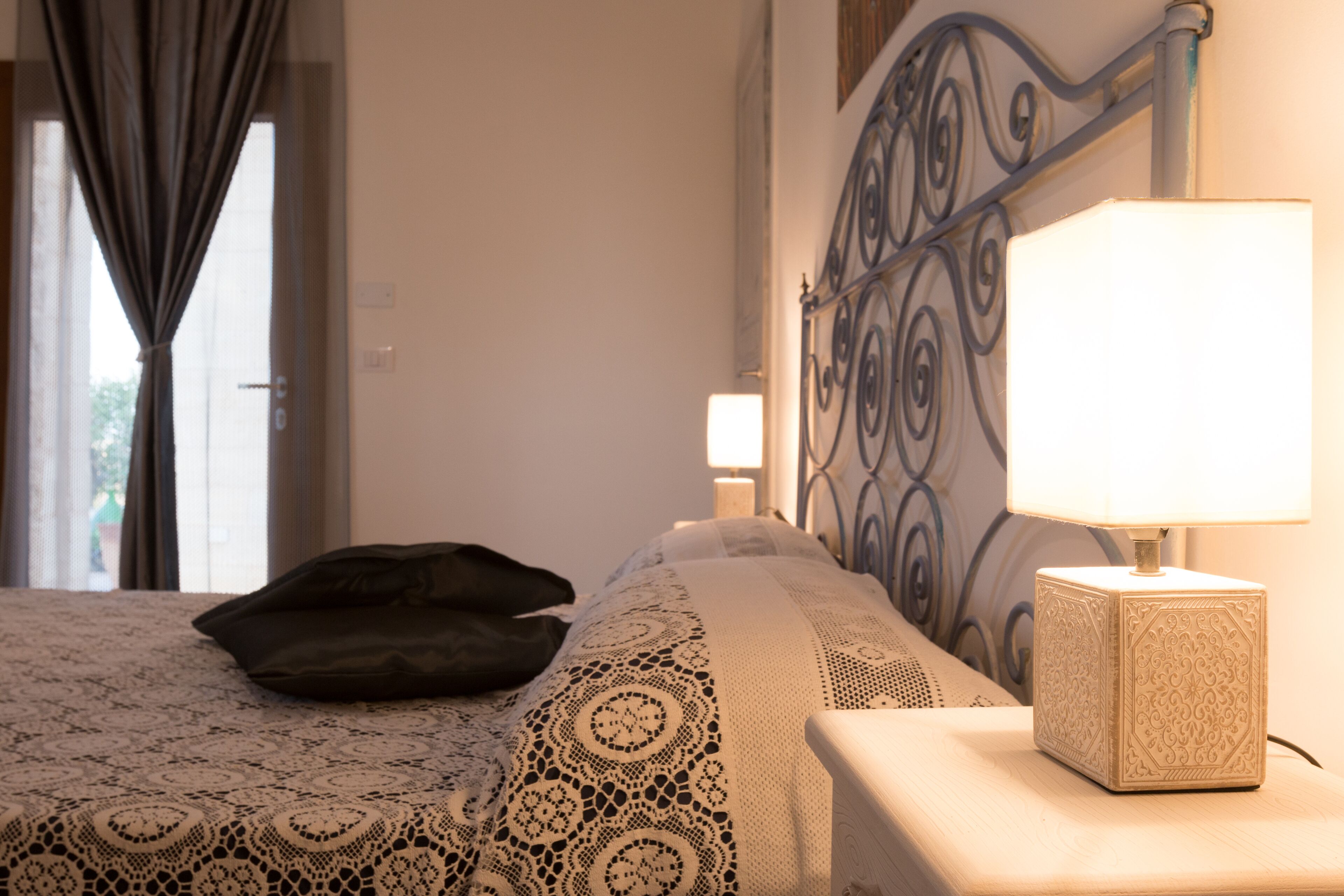 A neatly made bed with a lace cover, a bedside lamp, and a black pillow.