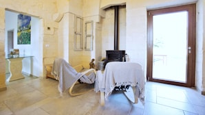 A room with stone walls, a fireplace, a rocking chair, and a table with a blanket. - Once Upon a Time in Masseria Sitamara (Lecce)