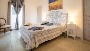 A bedroom with a bed, a chair, a nightstand, a lamp, and a door. - Once Upon a Time in Masseria Sitamara (Lecce)