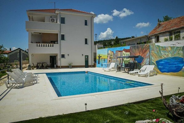 A two-story building with a swimming pool, lounge chairs, and a mural. - Imotski Blaue See Apartments , Pool (Imotski)
