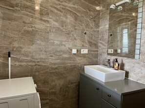 A bathroom with a marble wall, a white sink, a mirror, and a cabinet.