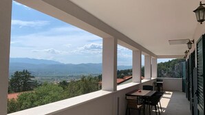 Een balkon met een tafel en stoelen, met uitzicht op verre bergen en een vallei.