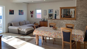 A modern living room with a sofa, dining table, and chairs. There are framed pictures on the walls and a window with a view. - "imotski Blaue See Apartments , Pool" (Imotski)