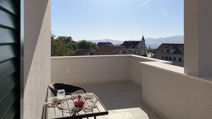 Un balcón con una mesa, una silla y vistas a edificios y montañas.
