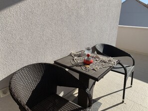 A small outdoor table with wicker chairs, a red object on the table, and a textured wall in the background.