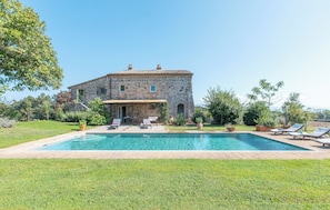 A stone building with a swimming pool, outdoor seating, and a well-maintained lawn.