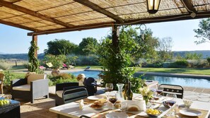 An outdoor dining area with a view of a swimming pool, surrounded by greenery and a clear sky. - Casa del Piano Valle dei Calanchi in Front of Civita Di Bagnoregio (Bagnoregio)