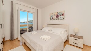 A bedroom with a bed, a nightstand, a painting, and a view of the sea. - Apartment by the sea and With Beautiful View, 2 Bedrooms, 4 Persons (Kali)