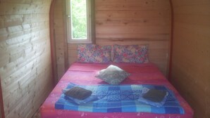 Una habitación pequeña y acogedora con paredes de madera, una ventana y una cama con ropa de cama estampada y una colcha.