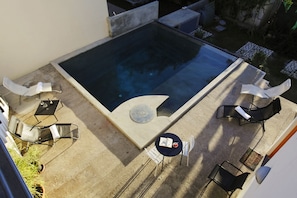 A rooftop pool area with a hot tub, surrounded by lounge chairs and a small table with a drink.