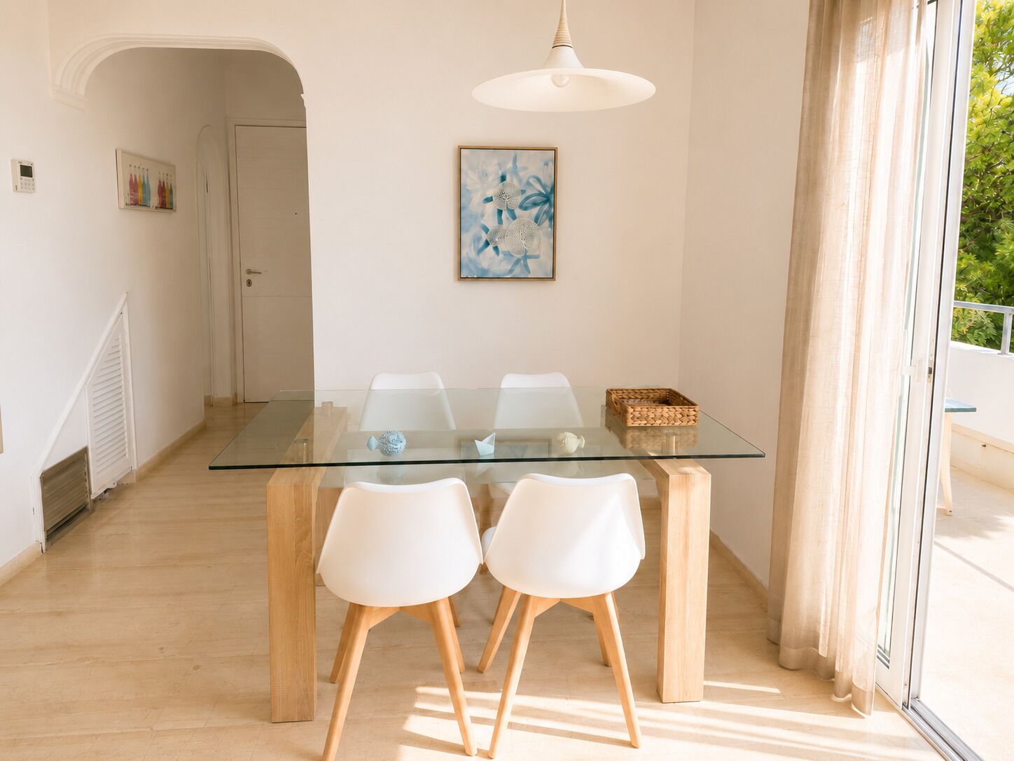 Un coin repas avec une table en verre et des chaises blanches, un luminaire au plafond et une porte donnant sur une autre pièce.