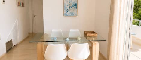 Un coin repas avec une table en verre et des chaises blanches, un luminaire au plafond et une porte donnant sur une autre pièce.