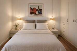 A bedroom with a bed, bedside tables, a nightstand with a plant, a framed picture on the wall, and a wardrobe with drawers. - Adelos Maisonette Near Vouliagmeni Beach (Vari-Voula-Vouliagmeni)
