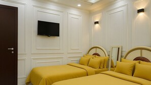 Ein Hotelzimmer mit zwei Betten, einem Deckenventilator, Einbaustrahlern, einem Flachbildfernseher und einer Tür.