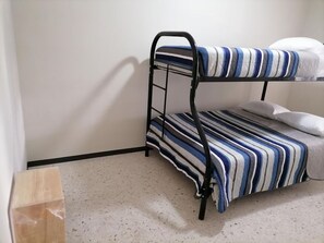 Een stapelbed met streepjesbeddengoed in een kamer met witte muren en een puntjesvloer.