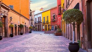 A cobblestone street with buildings on either side, some with balconies and potted plants.