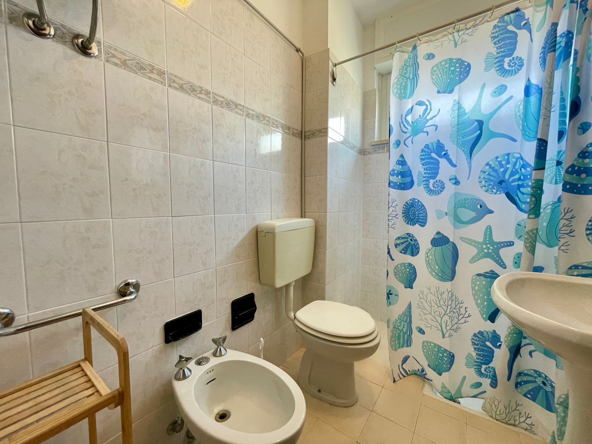 A bathroom with a bidet, toilet, and a shower curtain with a sea life pattern.