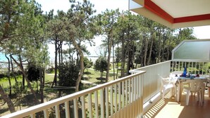A balcony with a white railing, a table with chairs, and a view of trees and a body of water. - Renovated Apartment With sea View Terrace (Caorle)