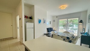 A compact kitchen with a refrigerator, a dining area with a table and chairs, and a view of the outdoors through a glass door. - Renovated Apartment With sea View Terrace (Caorle)