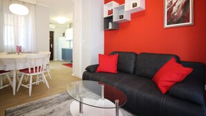 Een moderne woonkamer met een zwarte leren bank, rode kussens, een glazen salontafel en witte eetkamerstoelen.