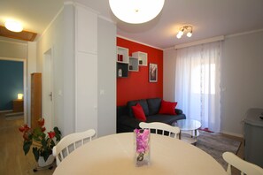 A modern living room with a red accent wall, white furniture, and a vase with flowers on a round table.