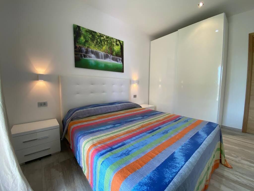 A bedroom with a large bed, a headboard, a nightstand, a drawer unit, and a wall-mounted painting of a waterfall.