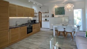 Eine moderne Küche mit Holzausstattung, einem Essbereich mit Glastisch und einem großen Fenster.