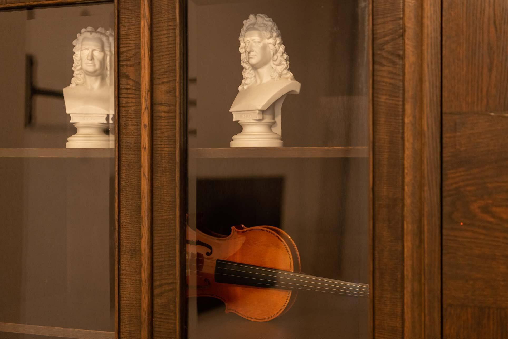 Un meuble en bois doté de portes en verre, contenant deux bustes et un violon.