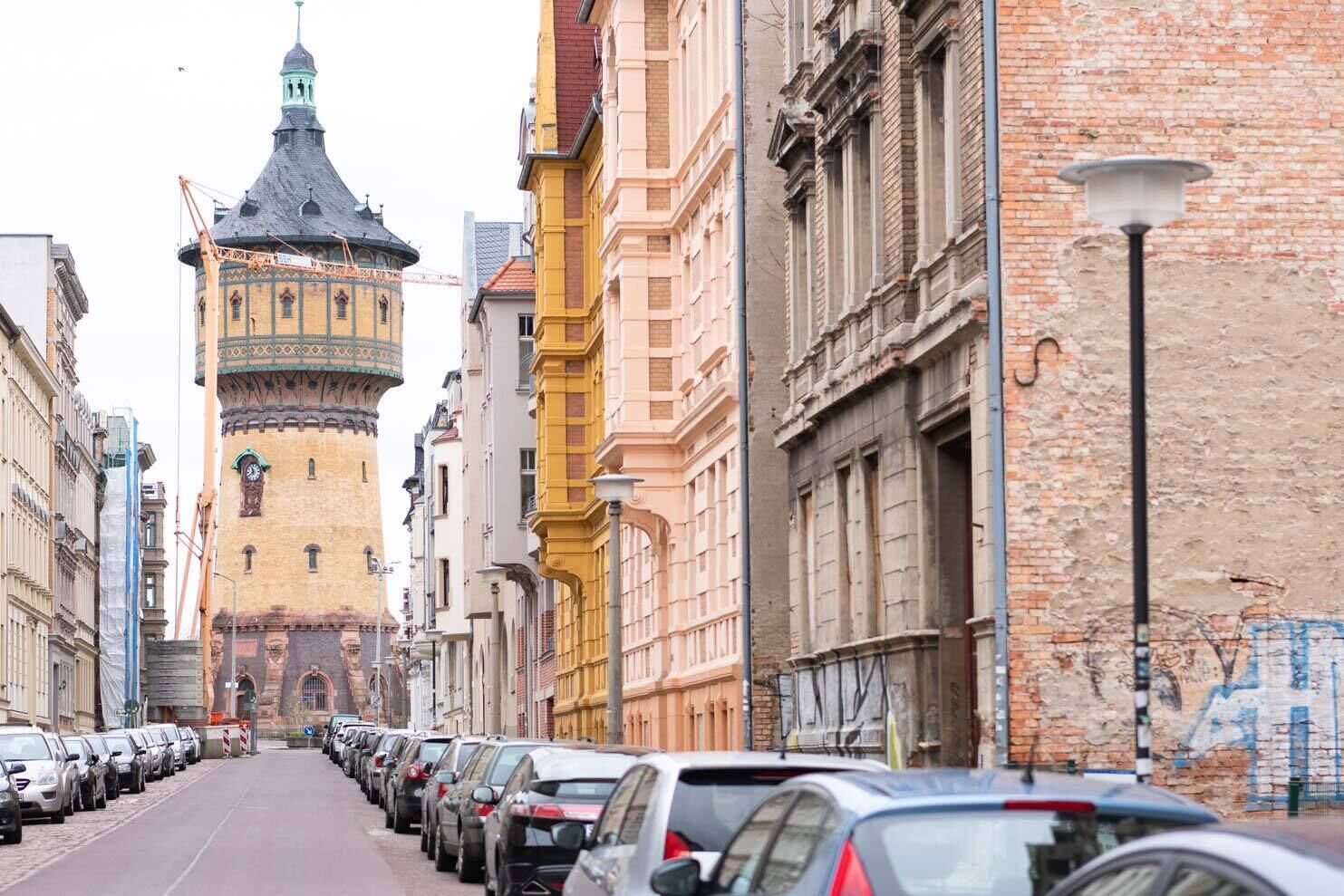 A street lined with parked cars and historic buildings, including a tower with a clock.