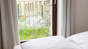 A hotel room with a bed and a window overlooking a balcony with a metal railing and greenery.