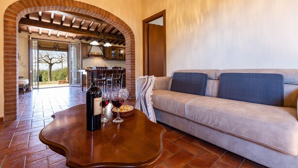 A cozy living room with a wooden coffee table, a beige sofa, and a brick archway leading to a dining area. - Captivating 1-bed Villa With Pool in Tuscany (Palaia)