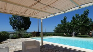 A covered outdoor area with a pool, stone flooring, and white wicker furniture. - Captivating 1-bed Villa With Pool in Tuscany (Palaia)