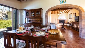 A dining area with a wooden table set for a meal, a brick fireplace, and a television in the background. - Captivating 1-bed Villa With Pool in Tuscany (Palaia)