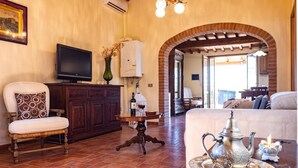 A living room with a television, a fireplace, and a dining table with a teapot. - Captivating 1-bed Villa With Pool in Tuscany (Palaia)