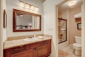 A bathroom with a granite countertop sink, wooden vanity, a large mirror with lights, a glass shower enclosure, and a toilet.