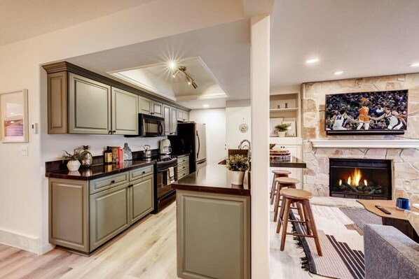 A modern kitchen with a central island, built-in appliances, and a stone fireplace. - The Wildflower | Lower DV 2BR, Private Hot Tub (Park City)