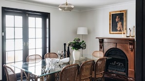 Uma sala de jantar com mesa de vidro, cadeiras de vime, lareira e um quadro na parede.