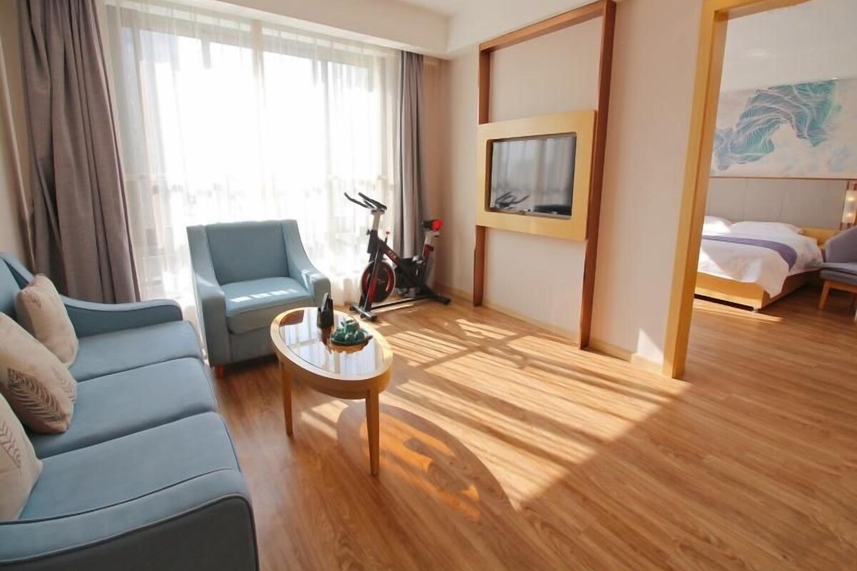 A hotel room with a sofa, a coffee table, a bike, a bed, and a painting on the wall.