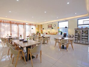 A spacious dining area with multiple tables and chairs, a kitchen in the background, and a refrigerator on the right.