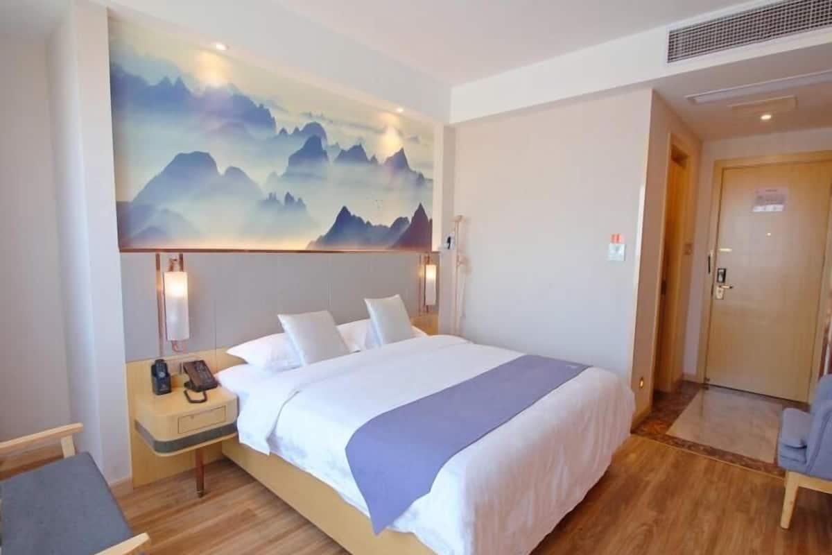 Ein Hotelzimmer mit einem großen Bett, einem Nachttisch mit Telefon, einem Schreibtisch mit Stuhl und einer Wand mit einem Bergpanorama.