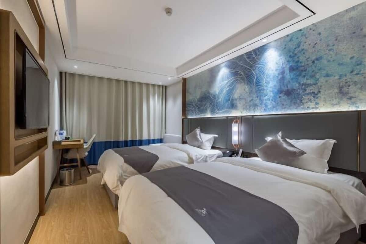 Ein Hotelzimmer mit zwei Betten, einem Schreibtisch, einem Sessel sowie einem großen, abstrakten Gemälde an der Wand und einem Fernseher.