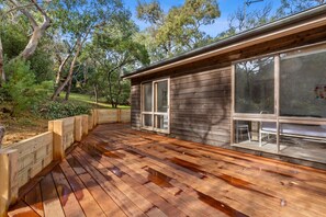 Eine Holzterrasse mit integriertem Sitzplatz, umgeben von einem Holzzaun und Bäumen.