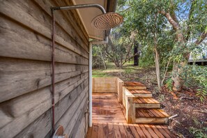 A wooden deck with a showerhead, surrounded by trees and a wooden bench.