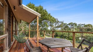 A wooden deck with a table and chairs, overlooking a natural landscape.